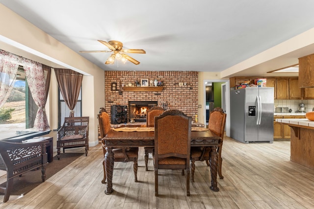 dining area with light hardwood / wood-style floors, a brick fireplace, and ceiling fan