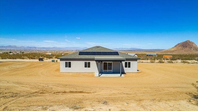 rear view of property featuring solar panels, a mountain view, and stucco siding