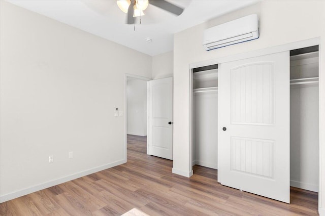 unfurnished bedroom with a closet, light wood-style flooring, a ceiling fan, a wall mounted air conditioner, and baseboards