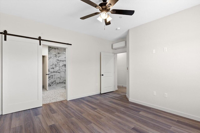 unfurnished bedroom featuring ceiling fan, a barn door, a wall unit AC, wood finished floors, and baseboards