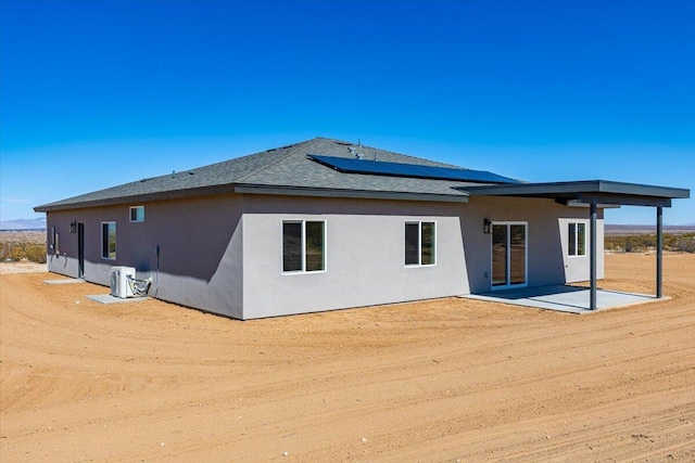 back of house featuring stucco siding, a shingled roof, roof mounted solar panels, a patio area, and cooling unit