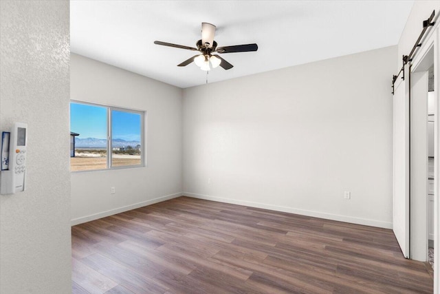 unfurnished bedroom with a ceiling fan, wood finished floors, baseboards, and a barn door