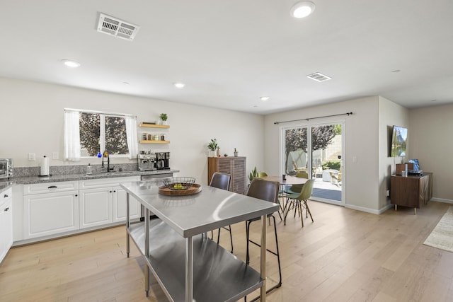 kitchen with light stone countertops, white cabinetry, sink, and light hardwood / wood-style flooring