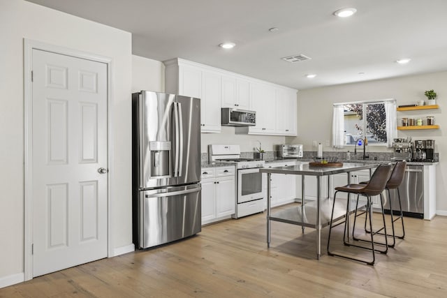 kitchen with a kitchen bar, white cabinets, light wood-type flooring, and appliances with stainless steel finishes