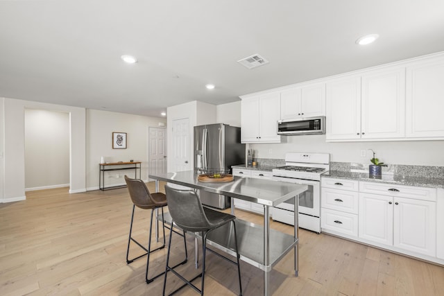 kitchen featuring light hardwood / wood-style floors, white cabinetry, light stone countertops, and appliances with stainless steel finishes