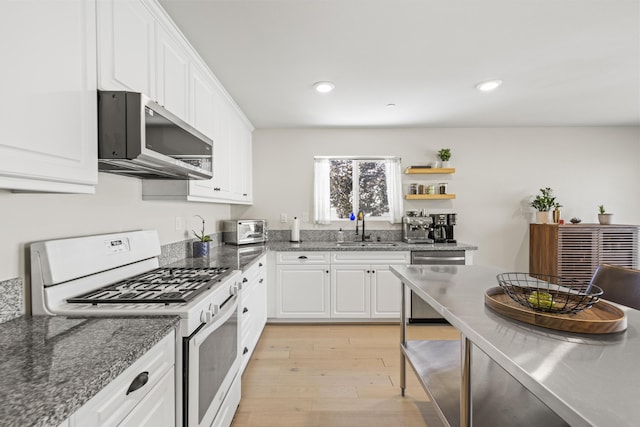 kitchen featuring sink, stainless steel appliances, dark stone countertops, light hardwood / wood-style floors, and white cabinets