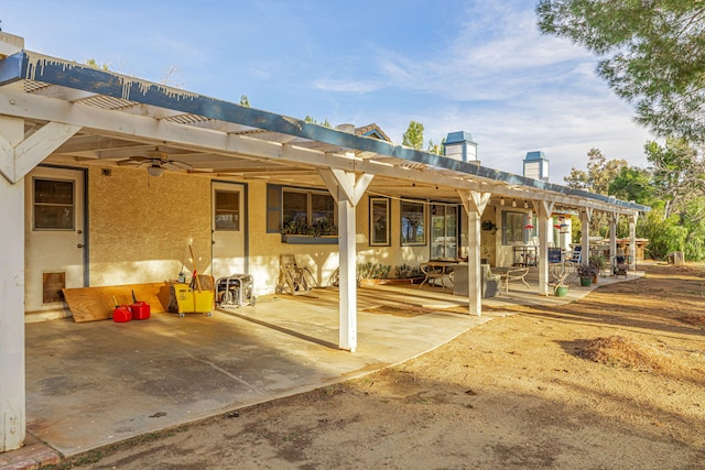 rear view of house featuring stucco siding, a ceiling fan, a pergola, and a patio