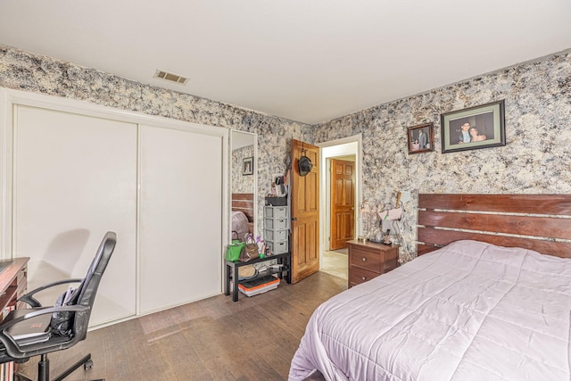 bedroom with dark wood-type flooring, a closet, visible vents, and wallpapered walls