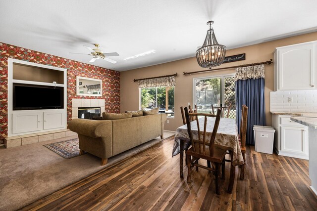 dining room featuring ceiling fan with notable chandelier, dark wood-type flooring, and a tiled fireplace