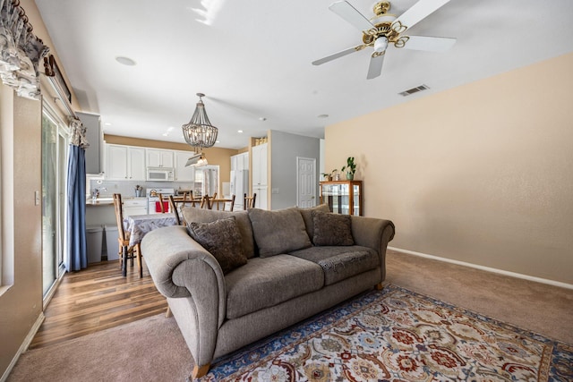 living room featuring ceiling fan with notable chandelier and light colored carpet