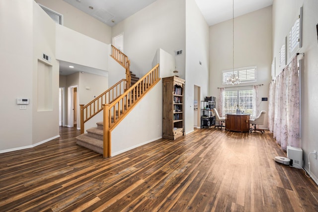 unfurnished living room with dark hardwood / wood-style flooring, a towering ceiling, and an inviting chandelier