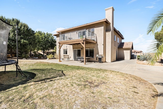 back of property with a patio, a trampoline, a balcony, and a lawn