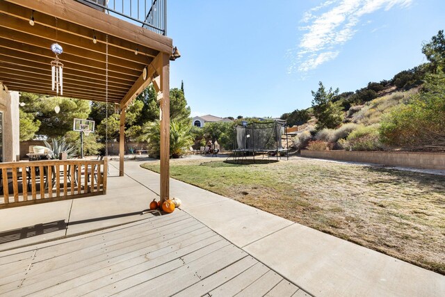 wooden terrace featuring a patio, a trampoline, and a lawn