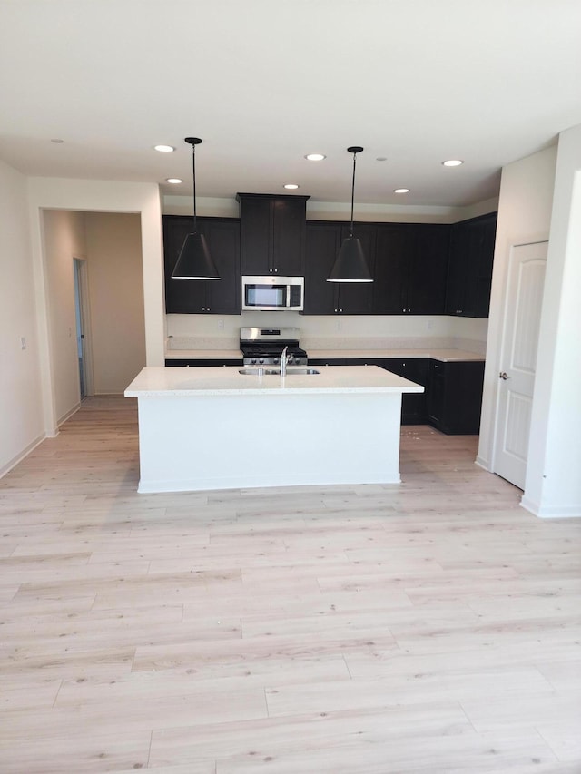 kitchen featuring light wood-type flooring, light countertops, dark cabinets, a sink, and stainless steel appliances