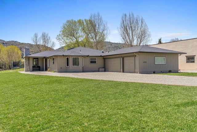 back of house featuring a yard, an attached garage, driveway, and a chimney