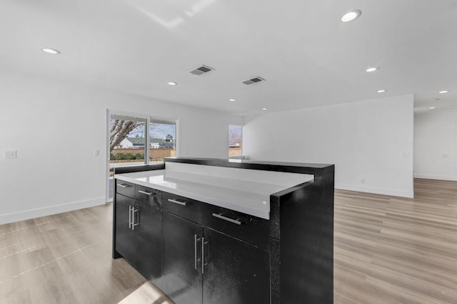 kitchen featuring visible vents, a kitchen island, dark cabinets, light countertops, and recessed lighting