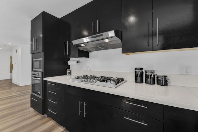 kitchen featuring modern cabinets, appliances with stainless steel finishes, dark cabinets, light countertops, and under cabinet range hood