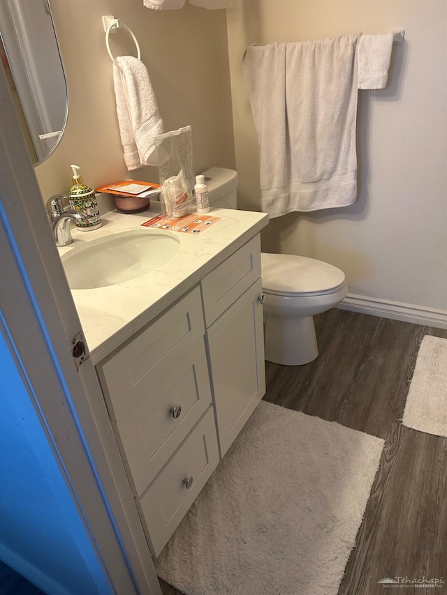 half bathroom with vanity, wood finished floors, and toilet