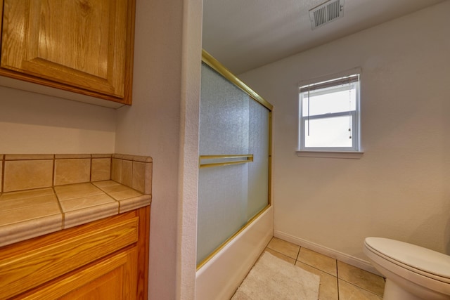 bathroom featuring toilet, tile patterned floors, shower / bath combination with glass door, and baseboards