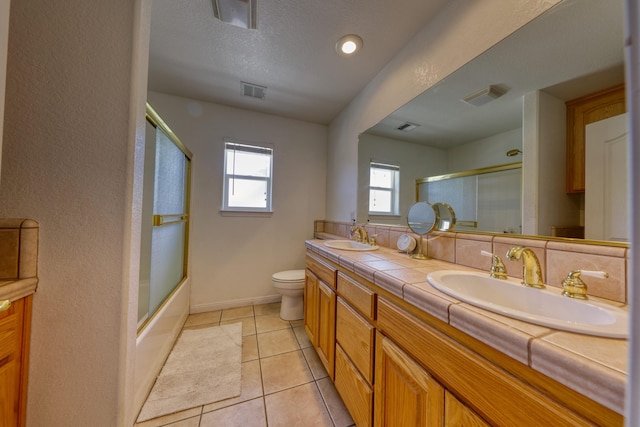 bathroom with double vanity, toilet, baseboards, tile patterned flooring, and enclosed tub / shower combo