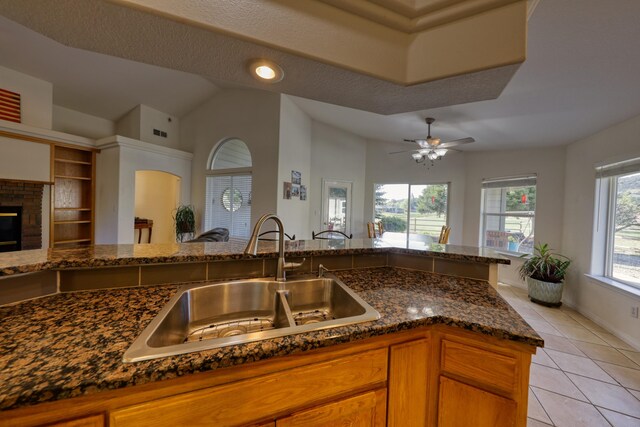 kitchen featuring a sink, light tile patterned flooring, dark stone countertops, open floor plan, and brown cabinets