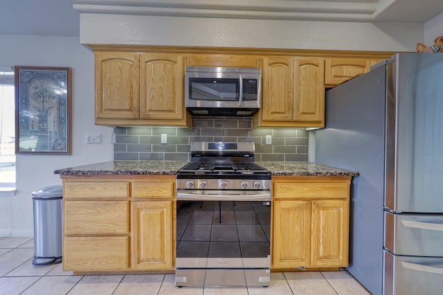 kitchen with appliances with stainless steel finishes, light tile patterned floors, tasteful backsplash, and dark stone counters