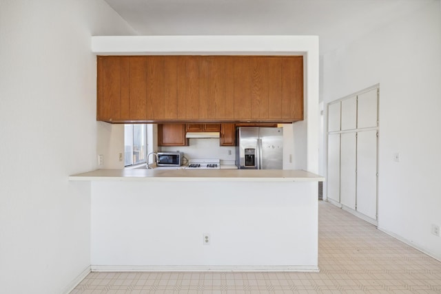 3112 Echo Dr, Rosamond, CA 93560 - kitchen featuring appliances with stainless steel finishes, light floors, under cabinet range hood, brown cabinets, and a peninsula