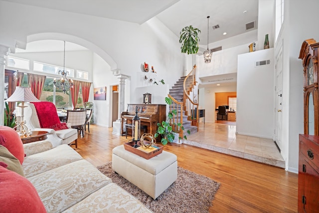 living room featuring decorative columns, wood-type flooring, high vaulted ceiling, and a chandelier