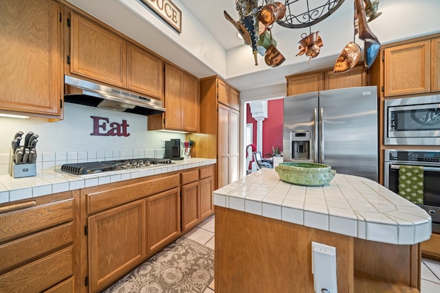 kitchen featuring light tile patterned floors, tile counters, stainless steel appliances, and a kitchen island