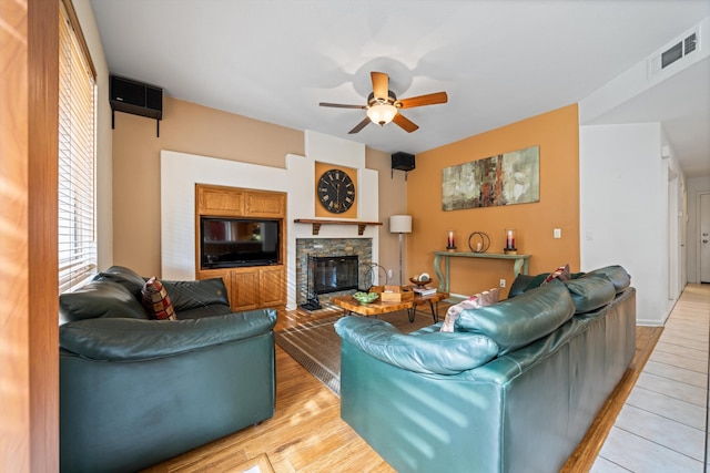 living room featuring ceiling fan, a fireplace, and light wood-type flooring