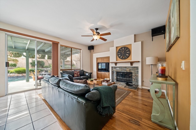 living room featuring ceiling fan, a stone fireplace, and light hardwood / wood-style floors