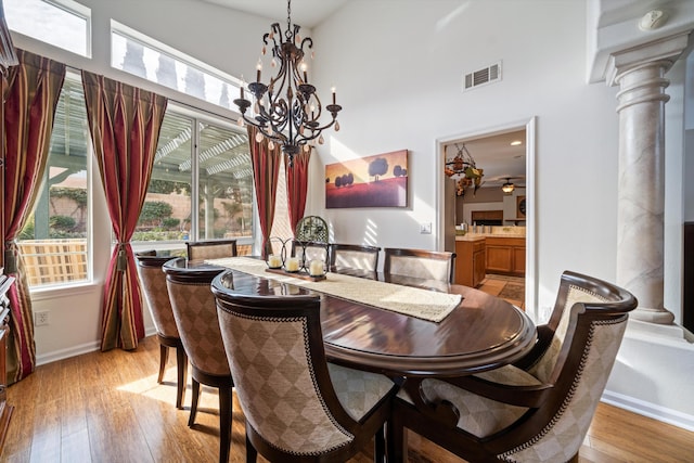 dining area featuring ceiling fan with notable chandelier, decorative columns, light hardwood / wood-style flooring, and a high ceiling