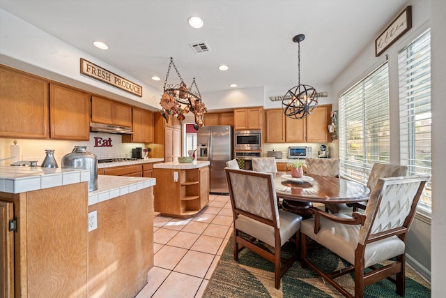 kitchen with tile countertops, decorative light fixtures, light tile patterned floors, a kitchen island, and stainless steel appliances