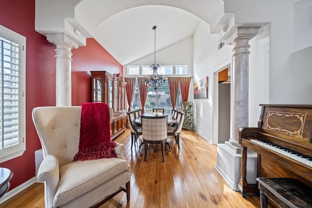 dining space featuring high vaulted ceiling, a chandelier, decorative columns, and light hardwood / wood-style flooring