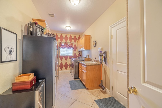 kitchen featuring washer and clothes dryer, sink, stainless steel fridge, light tile patterned floors, and a textured ceiling