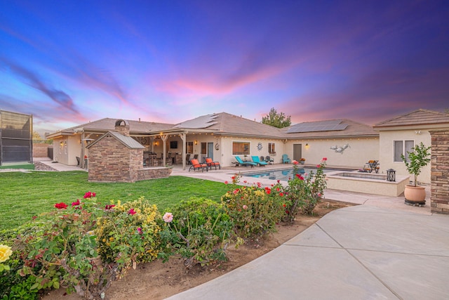 back house at dusk with a lawn, exterior kitchen, solar panels, an outdoor bar, and a patio