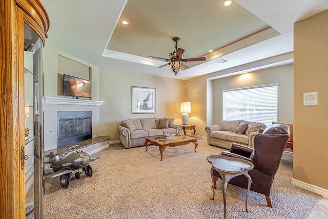 carpeted living room with a tray ceiling and ceiling fan