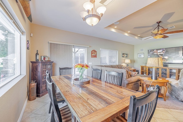 tiled dining space featuring a raised ceiling, a wealth of natural light, and ceiling fan with notable chandelier