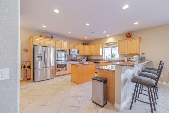 kitchen featuring sink, stainless steel appliances, light stone counters, kitchen peninsula, and a breakfast bar area