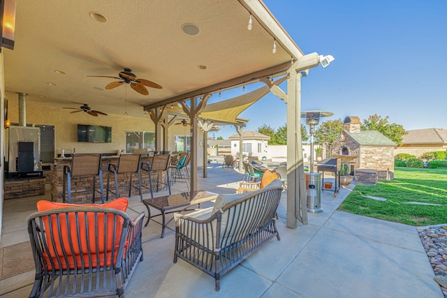 view of patio with an outdoor living space with a fireplace, ceiling fan, and a bar