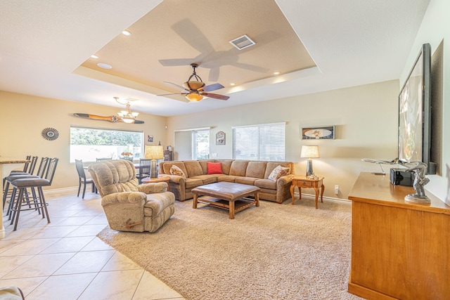 living room featuring a tray ceiling, light tile patterned floors, and ceiling fan with notable chandelier