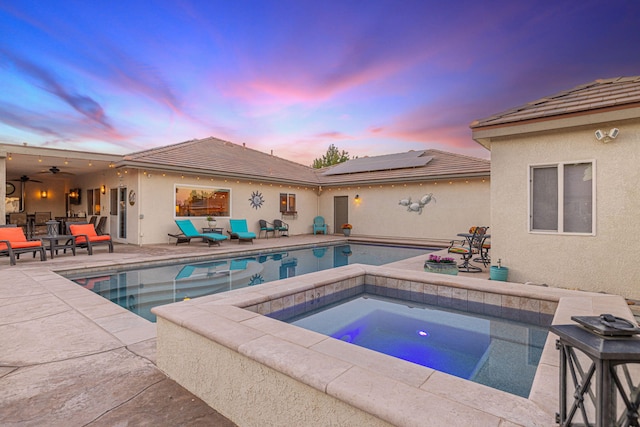 pool at dusk featuring an in ground hot tub and a patio