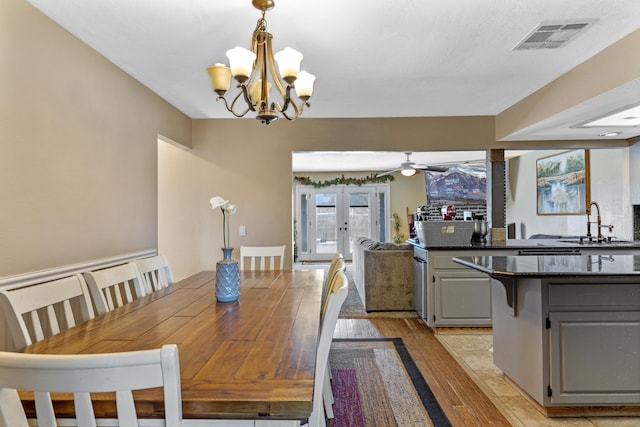 dining space with french doors, ceiling fan with notable chandelier, light hardwood / wood-style floors, and sink