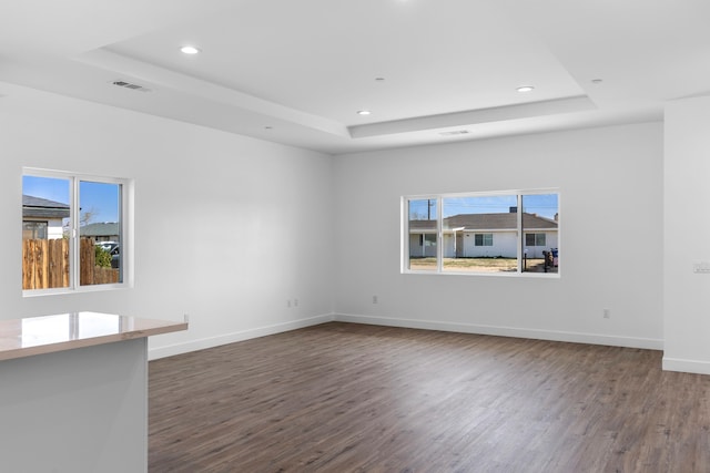 empty room featuring a raised ceiling, plenty of natural light, dark wood-style floors, and baseboards