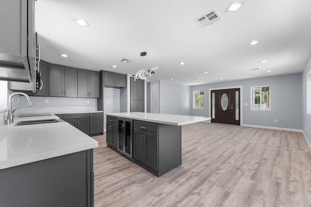 kitchen with decorative light fixtures, a kitchen island, light hardwood / wood-style floors, and beverage cooler