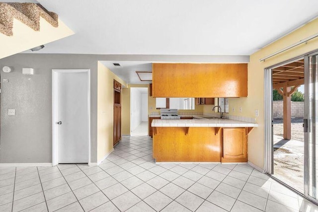 kitchen featuring a peninsula, stove, tile counters, brown cabinetry, and a kitchen bar