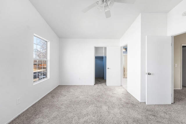 unfurnished bedroom featuring a walk in closet, a closet, light carpet, and ceiling fan