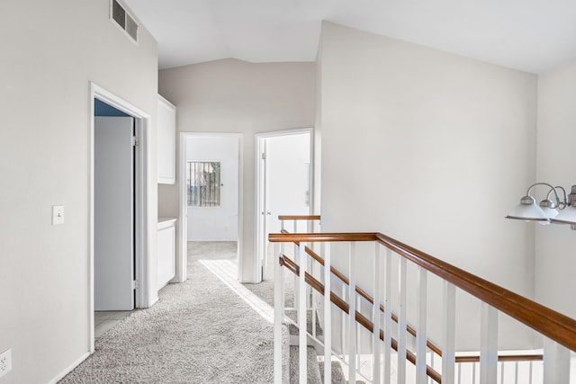 hall featuring light carpet, visible vents, vaulted ceiling, and an upstairs landing