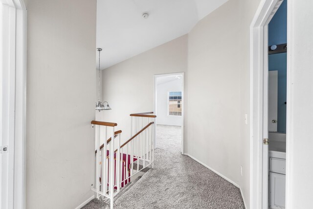 hall featuring lofted ceiling, carpet, baseboards, and an upstairs landing