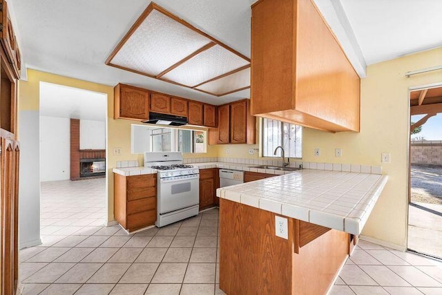 kitchen with a peninsula, white appliances, a sink, tile counters, and brown cabinetry